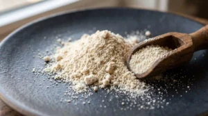 Macro close-up of beef bone broth protein powder on dark ceramic surface with wooden scoop