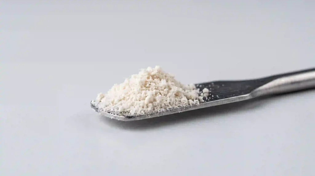Macro close‑up of off‑white hydrolyzed eggshell membrane peptide powder on a laboratory spatula