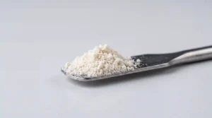 Macro close‑up of off‑white hydrolyzed eggshell membrane peptide powder on a laboratory spatula