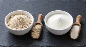 Beef protein isolate powder in a bowl next to whey protein isolate powder, comparing texture and color of the two protein supplements